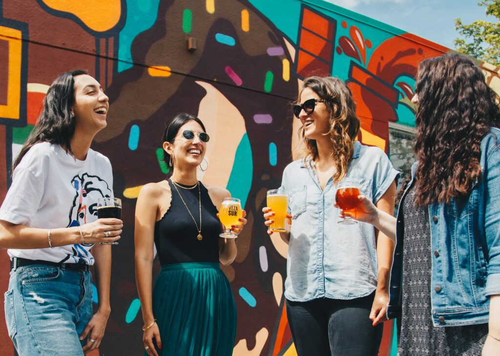 four women holding drinks against a graffiti painted wall