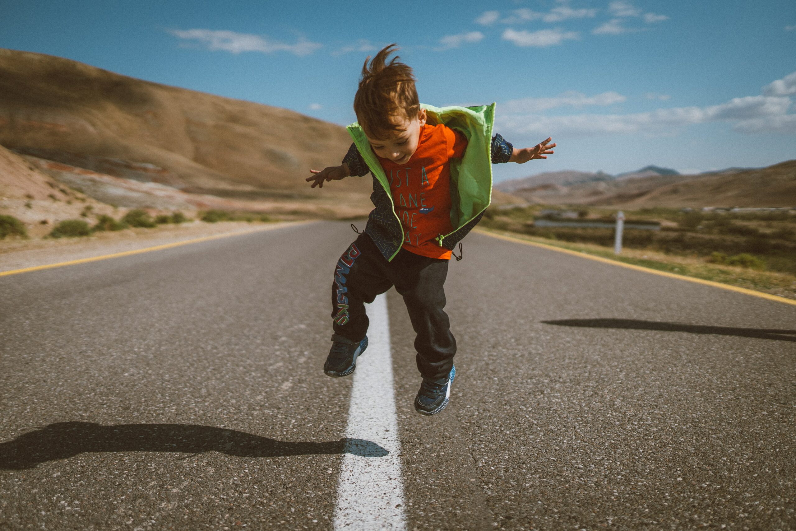 young kid jumping mid air in the middle of a country highway